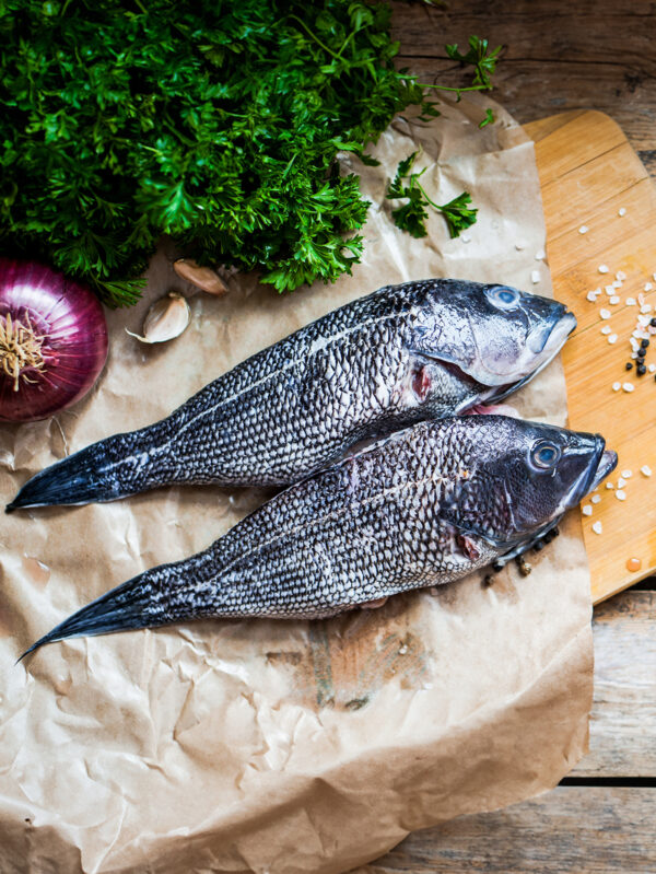 Fresh sea bass on board before preparation at wooden background