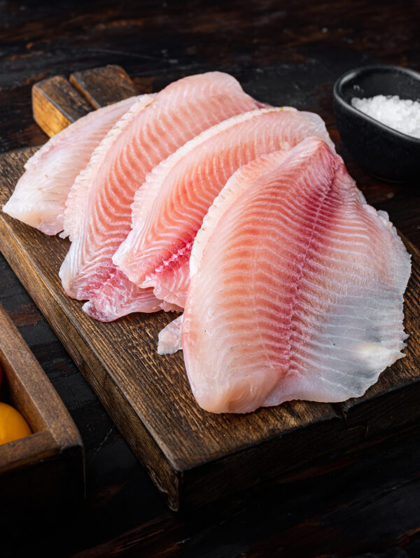 Raw white fish tilapia, with basmati rice and cherry tomatoes ingredients, on dark wooden background